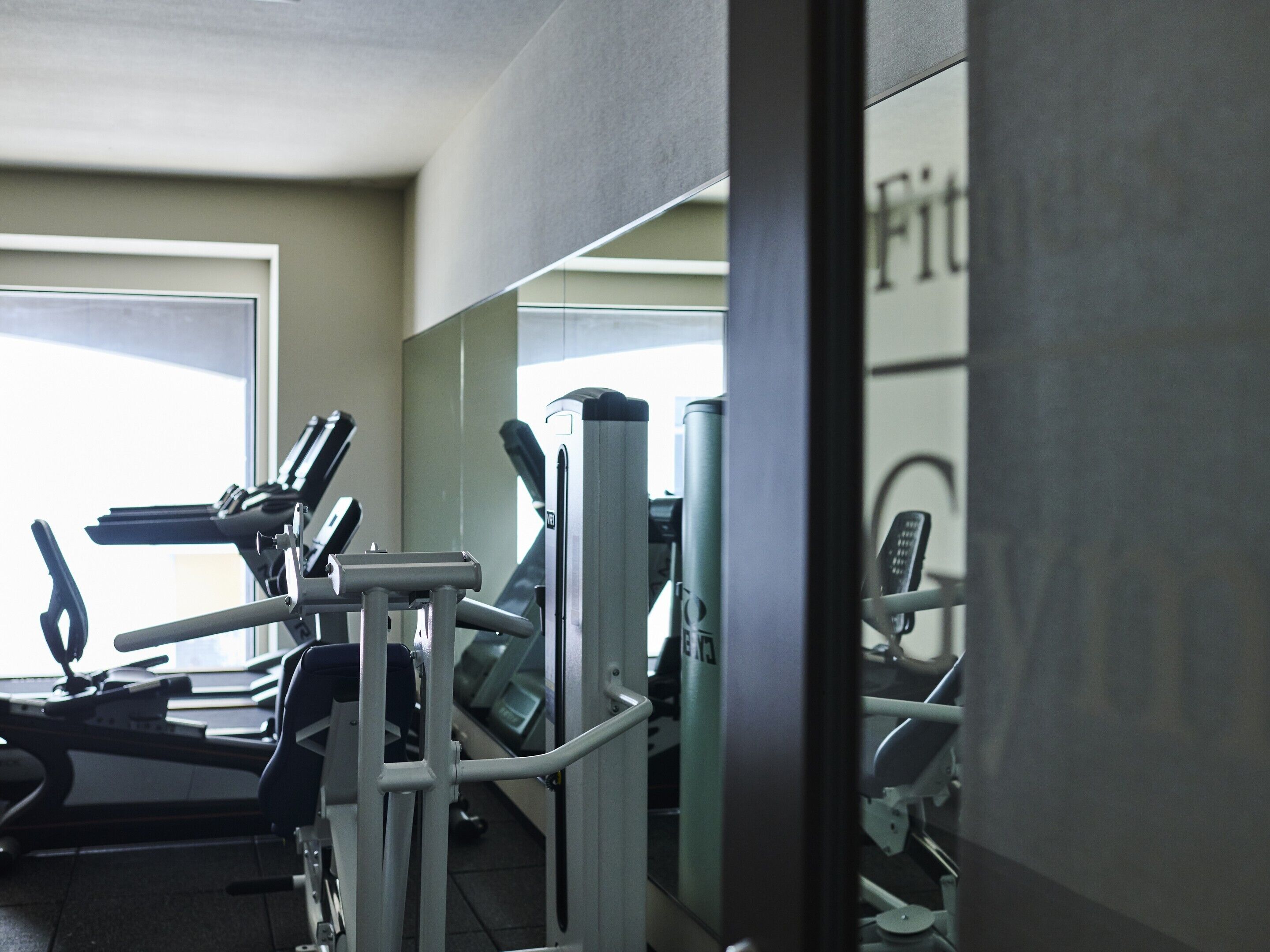 A gym with exercise equipment, a large mirror, and a window with natural light.