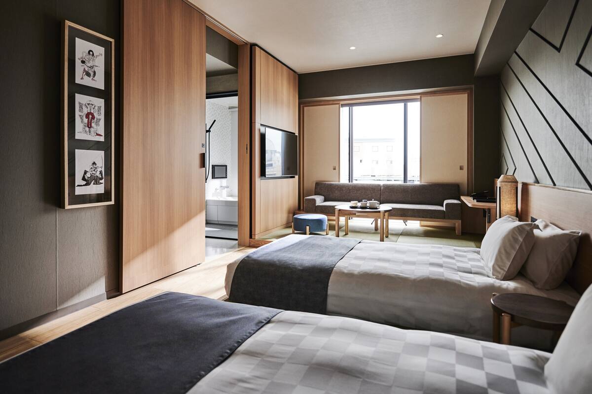 Una habitación de hotel moderna con dos camas, un sofá, un televisor y un ventanal grande.
