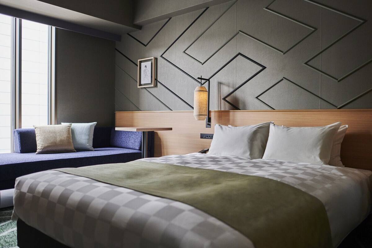Habitación de hotel con cama, sofá, pared con diseños geométricos y lámpara colgante.