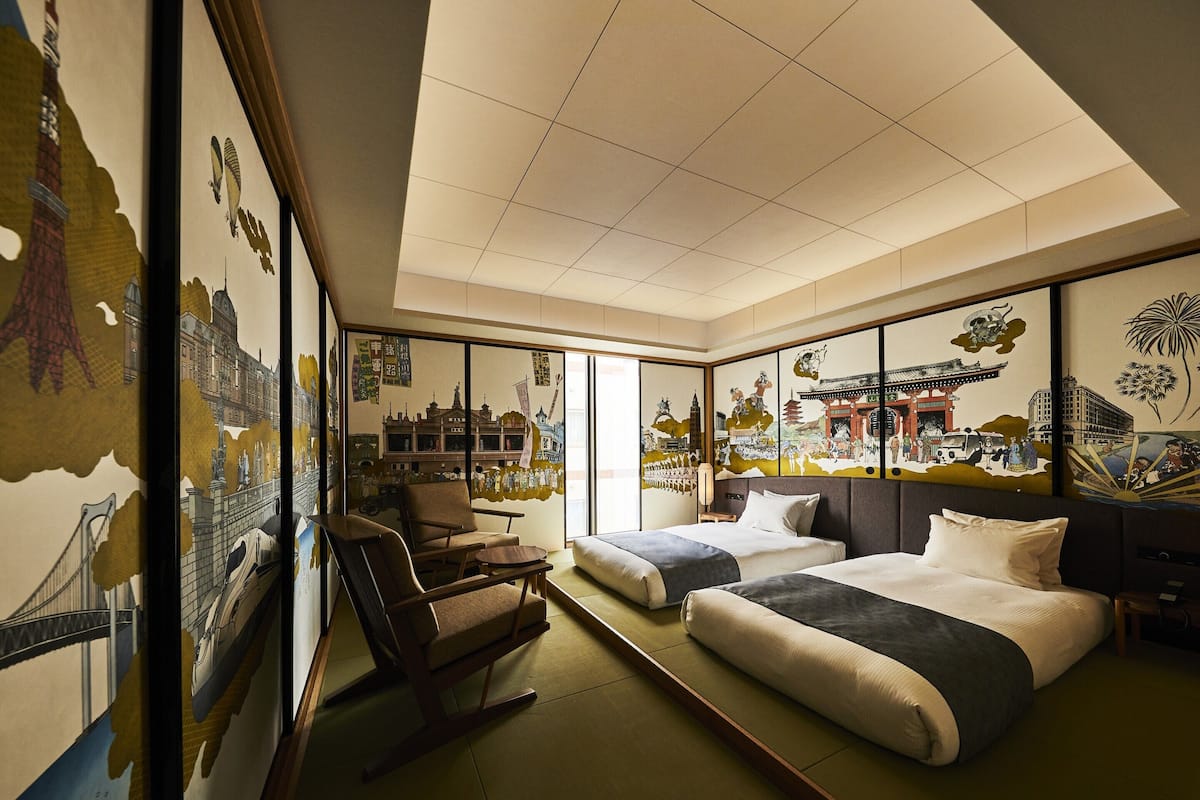 Habitación de hotel con dos camas, una silla y obras de arte que representan paisajes urbanos y escenas culturales.