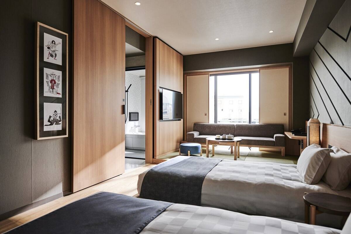 Una habitación de hotel moderna con dos camas, un sofá, un televisor y un ventanal amplio.