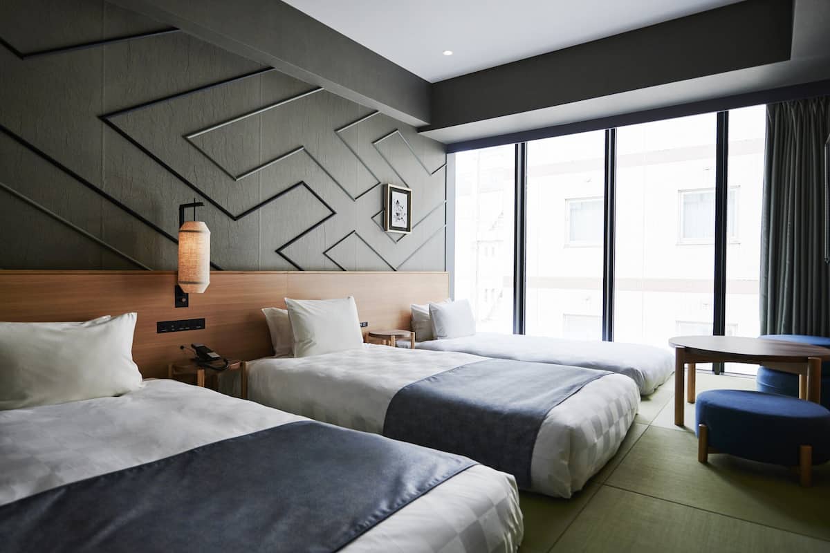 Habitación de hotel con dos camas, un escritorio y un ventanal grande.