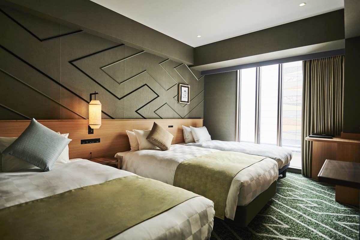 Habitación de hotel con dos camas, un ventanal con cortinas, una lámpara de pared y un diseño geométrico en la pared.
