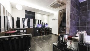 A modern hotel room with a black leather sofa, a desk with two monitors, a hairdryer, and a coffee machine. - Lexy Hotel (Daejeon)