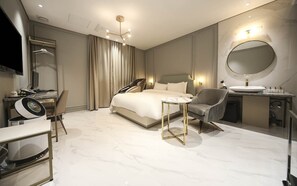 Une chambre d’hôtel moderne avec un grand lit, un miroir rond, une table de chevet, une chaise, un bureau avec un ordinateur et une salle de bain équipée d’un lavabo et d’un miroir.