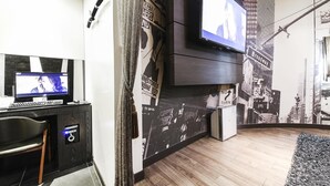 A modern living room with a flat-screen TV mounted on the wall, a desk with a computer, and a large poster of a cityscape. - Lexy Hotel (Daejeon)