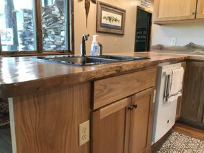 A kitchen with a granite countertop, wooden cabinets, a built-in dishwasher, and a stone backsplash. - The Cabin at Lowell (Garden City)