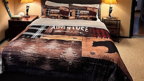 A bedroom with a large bed, two bedside tables with lamps, a ceiling fan, a wall-mounted shelf with decorative items, and a door leading to another room.