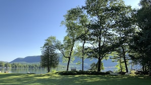 A grassy area with trees and a bench overlooking a lake with mountains in the background.