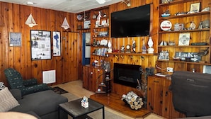 A cozy living room with wooden paneling, a fireplace, a flat-screen TV, and various decorative items on shelves.