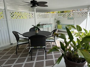 Ein überdachter Patio-Bereich mit rundem Tisch und Stühlen, einem Deckenventilator und Topfpflanzen.