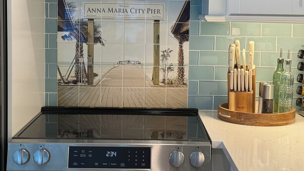 Una cocina con un reloj digital que marca las 2:34, una estufa y un salpicadero de azulejos con una escena de playa.