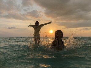 Zwei Personen im Meer, während die Sonne untergeht.