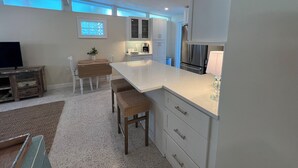 Una cocina moderna con armarios blancos, una isla central y un comedor con mesa y sillas.