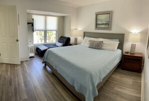 A bedroom with a bed, bedside lamps, a chair, a window, and a painting on the wall.