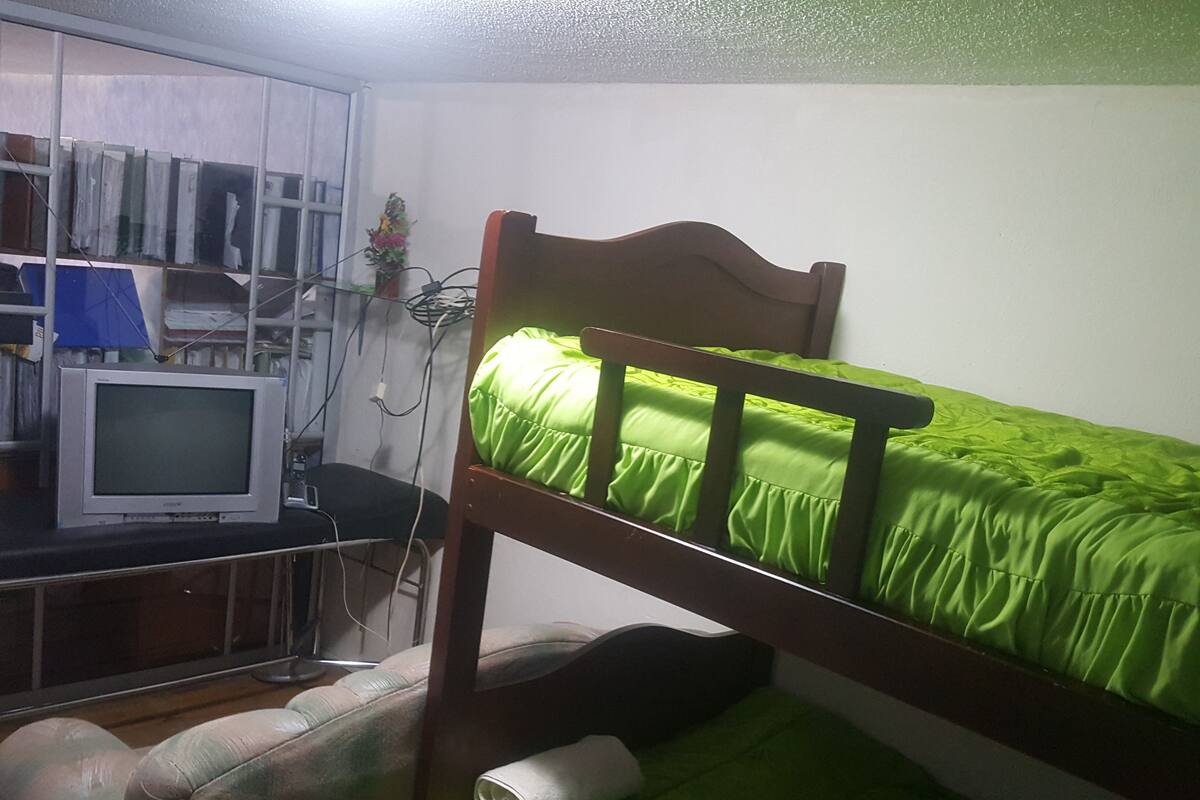 A dormitory room with a bunk bed, a desk with a computer, and a chair.