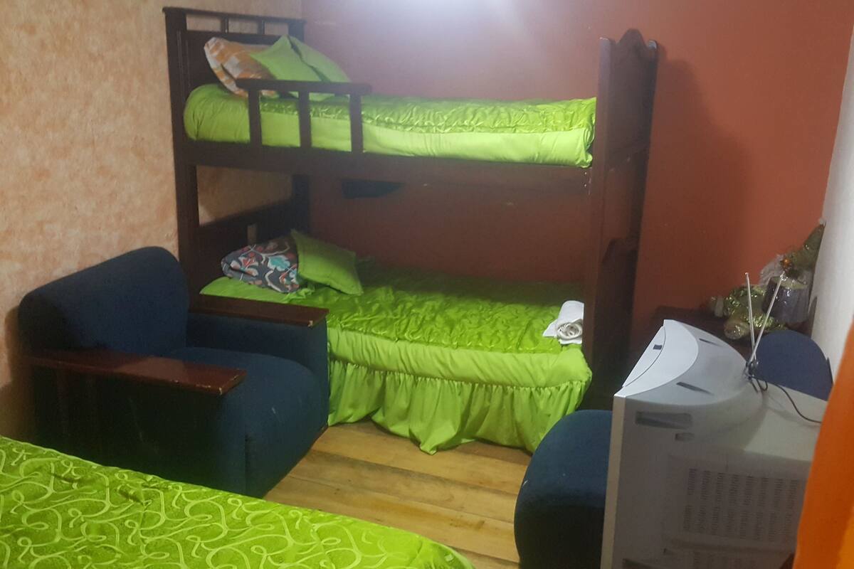 A bunk bed room with a desk and a chair, a television, and a patterned bedspread.