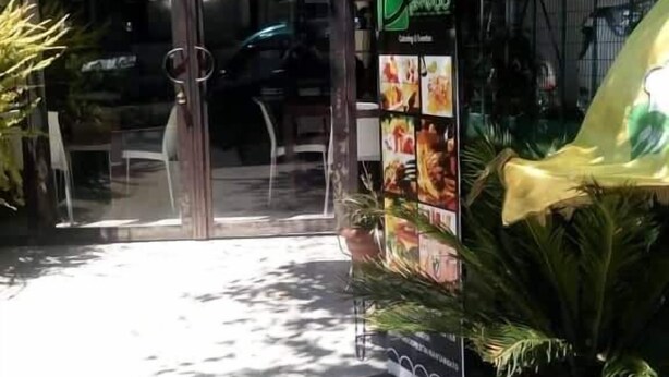 A restaurant with a glass entrance, outdoor seating, and a signboard with food images. - Bio Bamboo Bed and Breakfast (Ambato)