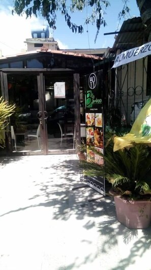A restaurant with a glass entrance, outdoor seating, and a signboard with food images. - Bio Bamboo Bed and Breakfast (Ambato)