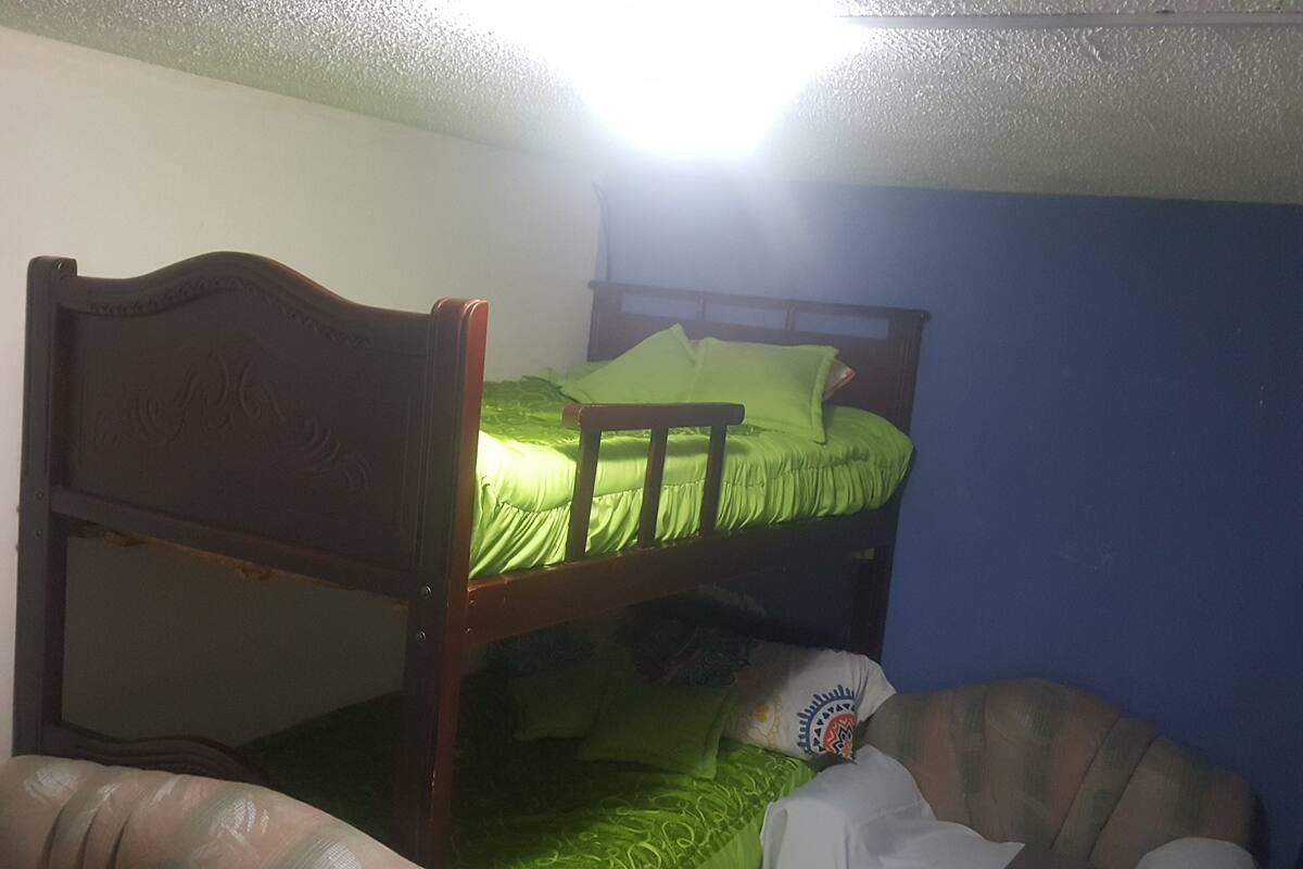 A bunk bed with a green mattress and pillows, a wooden headboard, and a white blanket on the lower bunk.