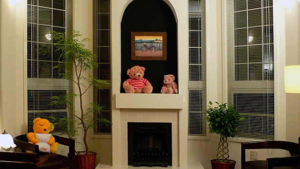 Un salon avec une cheminée, deux ours en peluche, une plante en pot et une lampe.