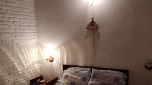 Ein Schlafzimmer mit Backsteinwand, einem Bett mit gemusterten Betttextilien, einer Hängeleuchte und einem kleinen Tisch mit einer Lampe.