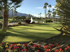 Un parcours de golf bien entretenu, agrémenté d’un étang, de palmiers et d’une montagne en arrière-plan.