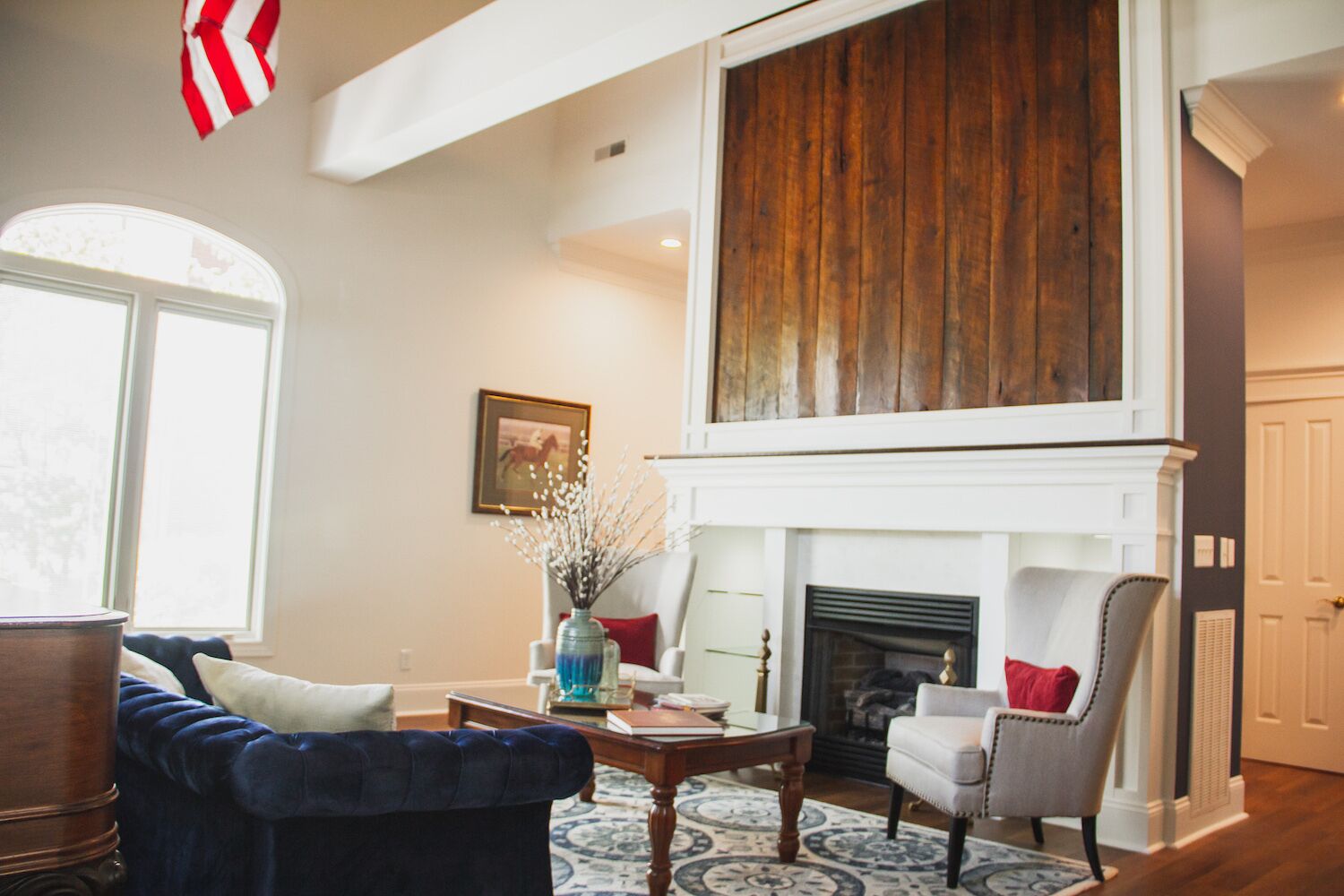 A spacious living room with a fireplace, a blue sofa, a grey armchair, and a wooden coffee table.