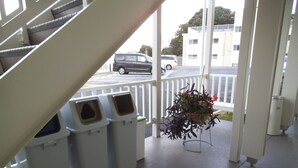 Un escalier menant à un balcon où se trouvent des poubelles et un pot de fleurs suspendu.