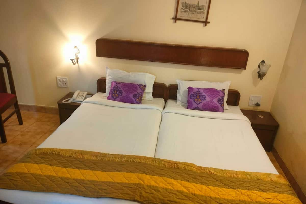 A double bed with a yellow quilt, two purple pillows, a wooden headboard, bedside lamps, and a framed picture on the wall.