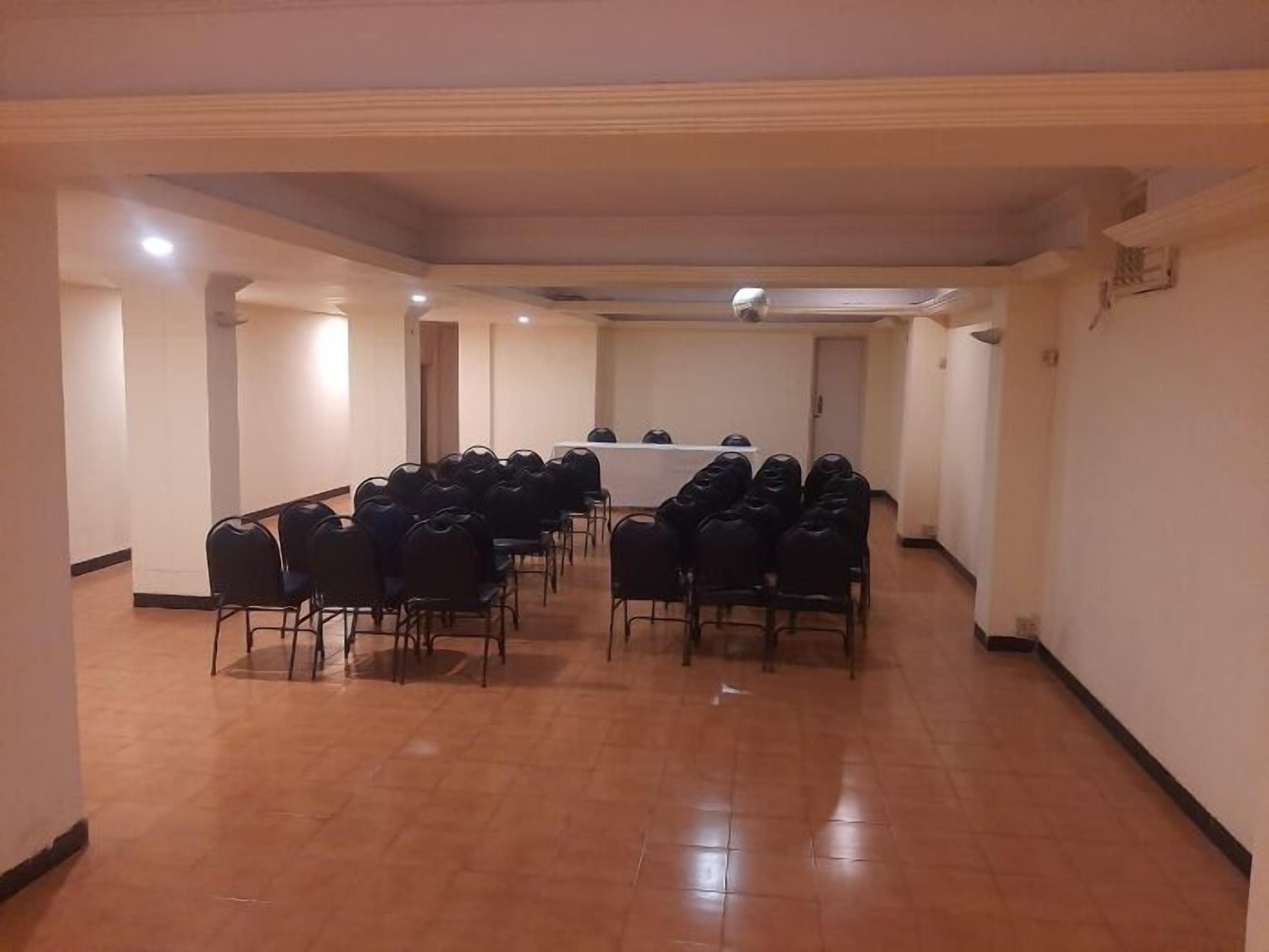 A conference room with rows of black chairs facing a white table with a projector.