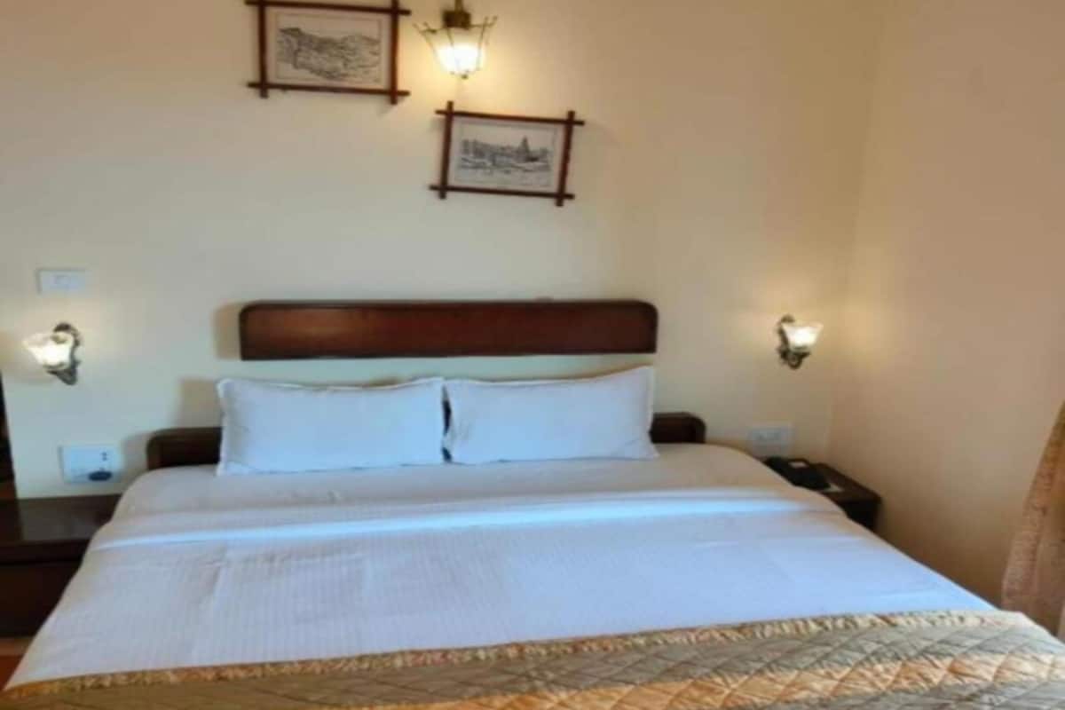 A hotel room with a bed, a nightstand, an air conditioning unit, and two wall-mounted lamps.
