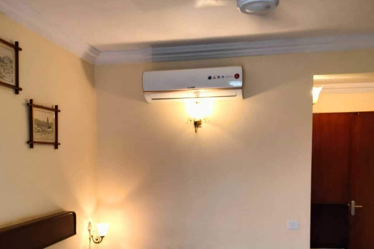 A hotel room with a bed, a ceiling fan, an air conditioning unit, and a wall-mounted light fixture.