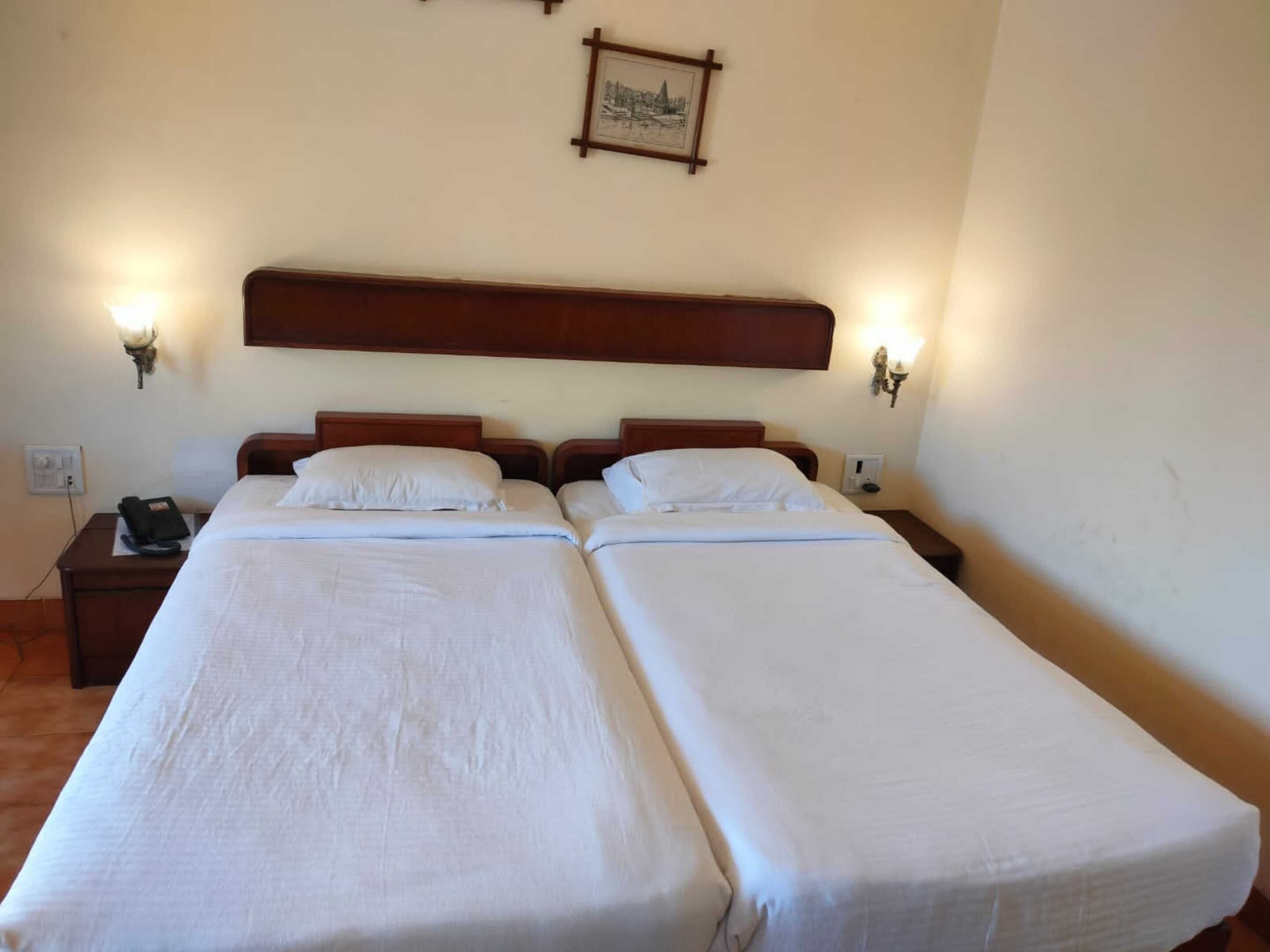 Habitación doble con dos mesitas de noche, cabecera y lámparas de pared.
