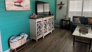 A living room with teal walls, a white cabinet, a television, a sofa, and a coffee table. - Reel’em Inn - a Waterfront Home on the Canal (Aransas Pass)