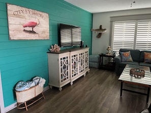 A living room with teal walls, a white cabinet, a television, a sofa, and a coffee table. - Reel’em Inn - a Waterfront Home on the Canal (Aransas Pass)