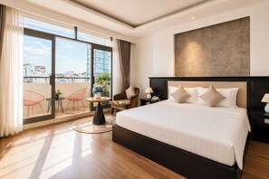 Ein Hotelzimmer mit großem Bett, Blick auf die Stadt durch raumhohe Fenster, einem runden Tisch mit Stühlen und einem modernen Kopfteil.