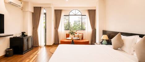 A hotel room with a large bed, a TV, a small table with a vase, and a view through a window.