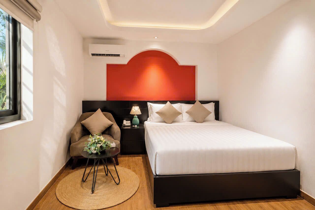 A modern hotel room with a bed, a nightstand, a lamp, a chair, and a small table with a vase of flowers.
