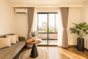 Une chambre dâhĂŽtel moderne avec un canapĂ©, une table ronde agrĂ©mentĂ©e dâun vase de fleurs, une plante en pot et une vue sur la ville grĂące Ă de grandes fenĂȘtres.