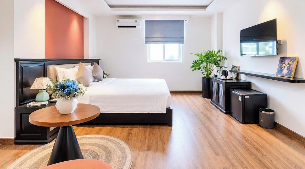 Ein modernes Hotelzimmer mit Bett, Nachttisch, Lampe und einem kleinen runden Tisch mit Blumenvase.