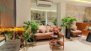 Un espace de détente moderne comprenant un canapé, un fauteuil et une table basse, le tout agrémenté de plantes en pot et d’une lampe décorative.