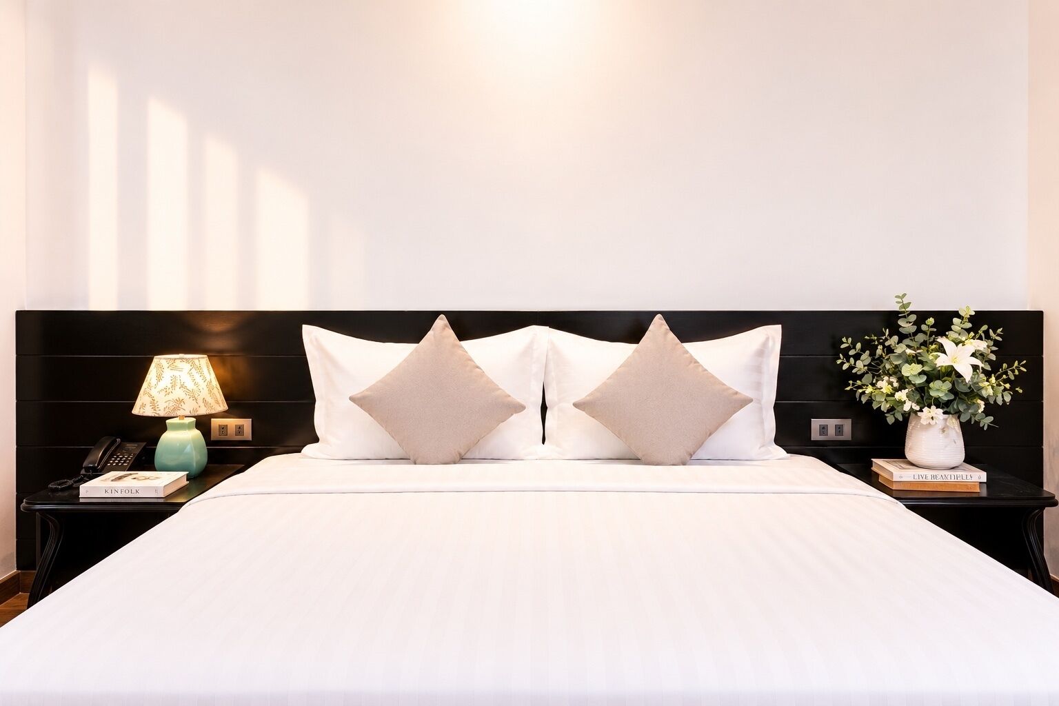 Habitación de hotel con una cama grande, dos mesitas de noche, una lámpara, un jarrón con flores y un libro titulado 'KINFOLK'.