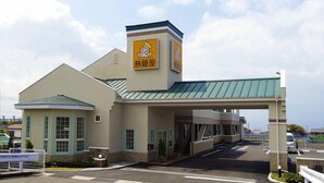 A building with a sign featuring a cartoon bear and Japanese characters, a covered entrance, and a parking lot. - Family Lodge Hatagoya Kagoshimatarumizu (Tarumizu)