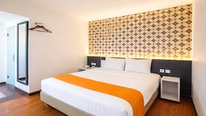 Une chambre d’hôtel moderne avec un grand lit, une tête de lit à motifs, des tables de chevet et une porte dotée d’un miroir.