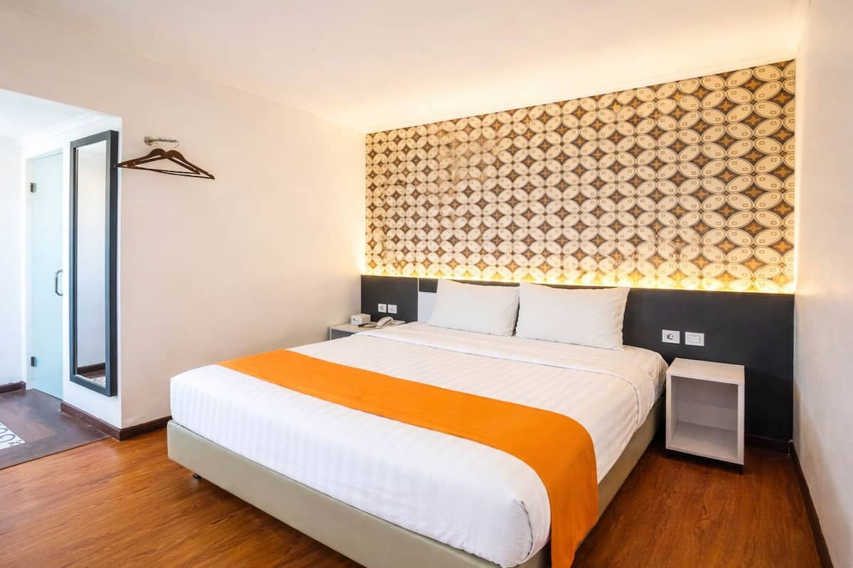 A modern hotel room with a large bed, a patterned headboard, bedside tables, and a door with a mirror.