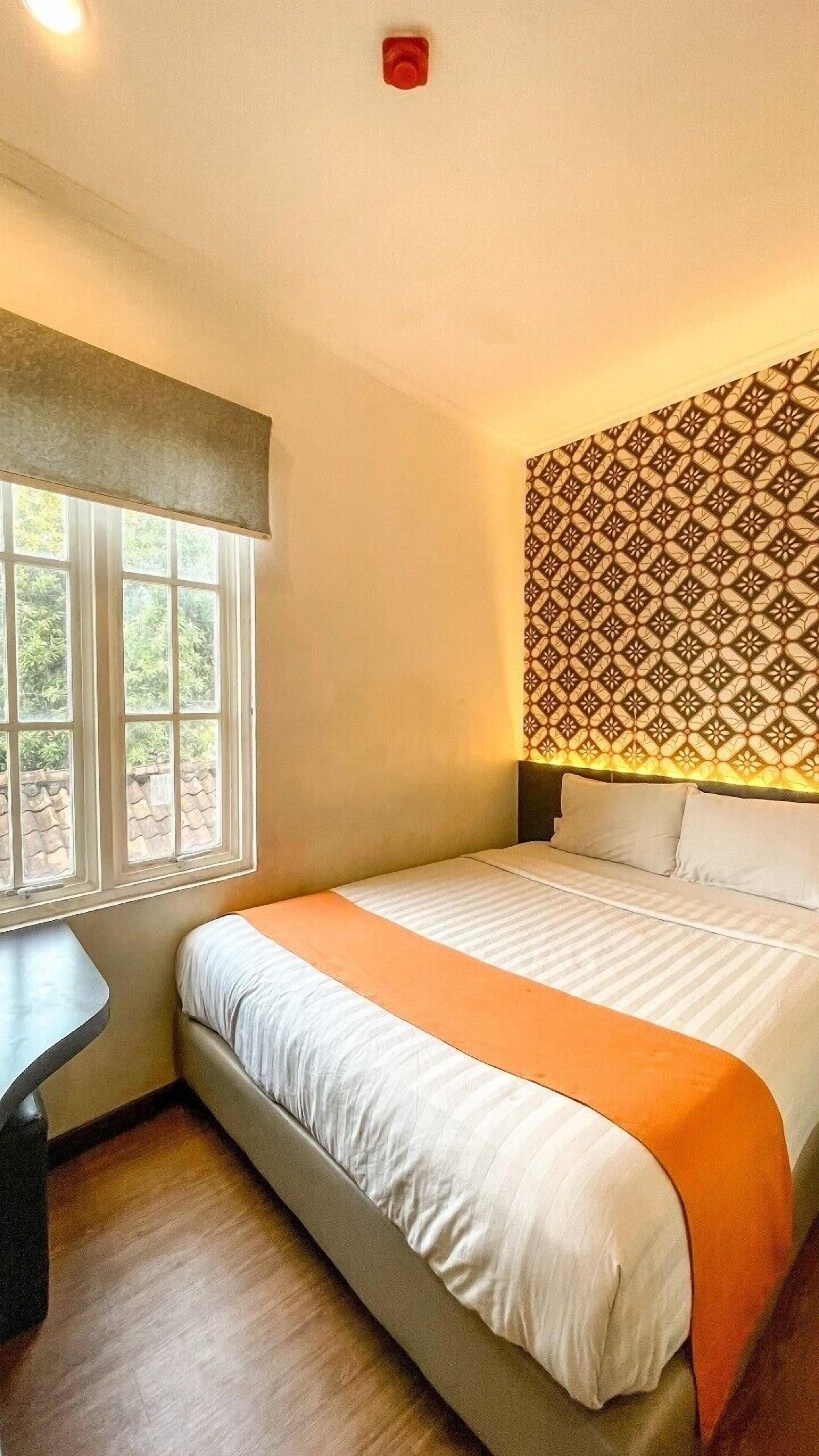 A hotel room with a bed, a desk, and a window.