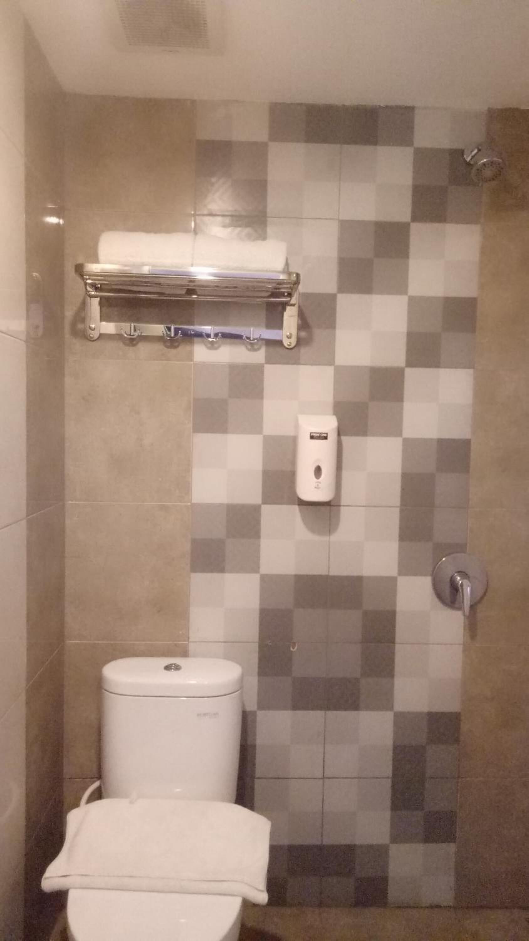 Un baño con inodoro, secamanos y cabezal de ducha.