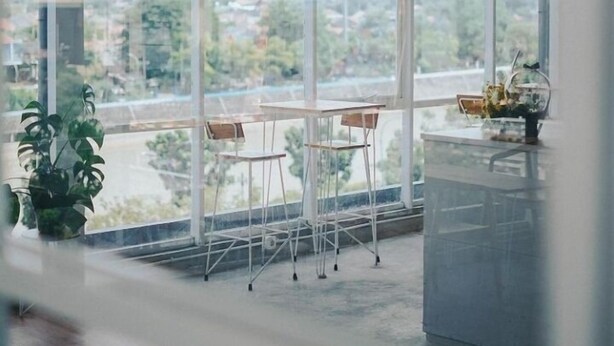 Il s’agit d’une pièce spacieuse avec de grandes fenêtres donnant sur un paysage urbain. On y trouve deux fauteuils et une petite table placés au centre.