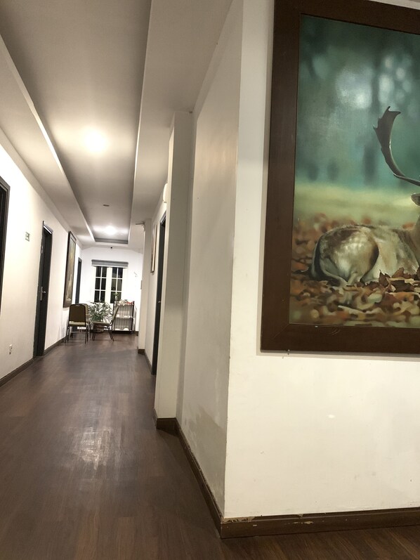 A hallway with a framed painting of a deer on the wall, wooden flooring, and a dining area with chairs and a table in the distance.